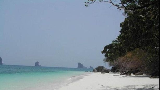 A beach with clear turquoise water, white sand, and rocky outcrops in the distance. - J Hotel (Krabi)