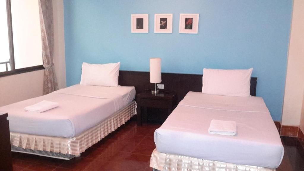 A hotel room with two beds, a nightstand with a lamp, and a window with curtains.