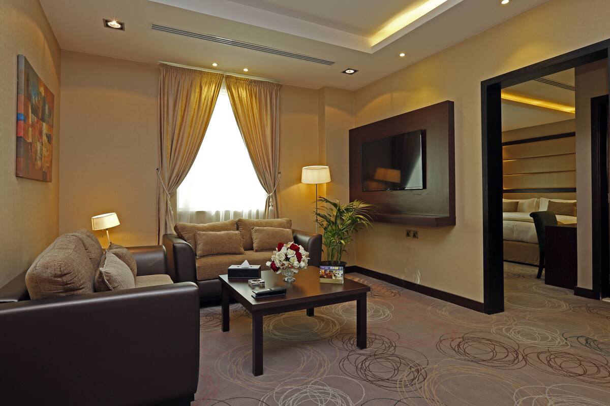 A hotel room with a sofa, armchairs, a coffee table, a TV, and a large mirror.