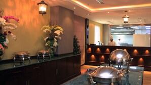 A hotel reception area with a counter, decorative flowers, and a kitchen in the background. - Swiss Flora Inn Hotel Riyadh (Riyadh)