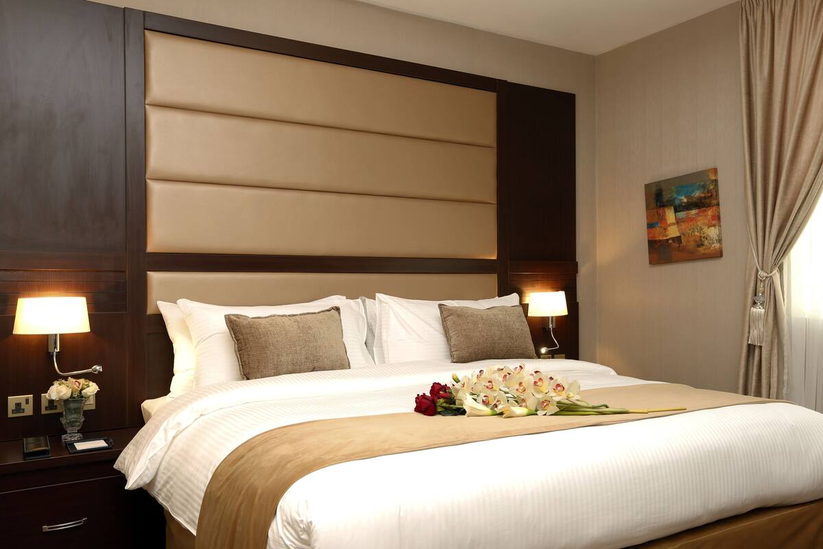 A hotel room with a large bed, two bedside tables, a nightstand, and a wall-mounted lamp.