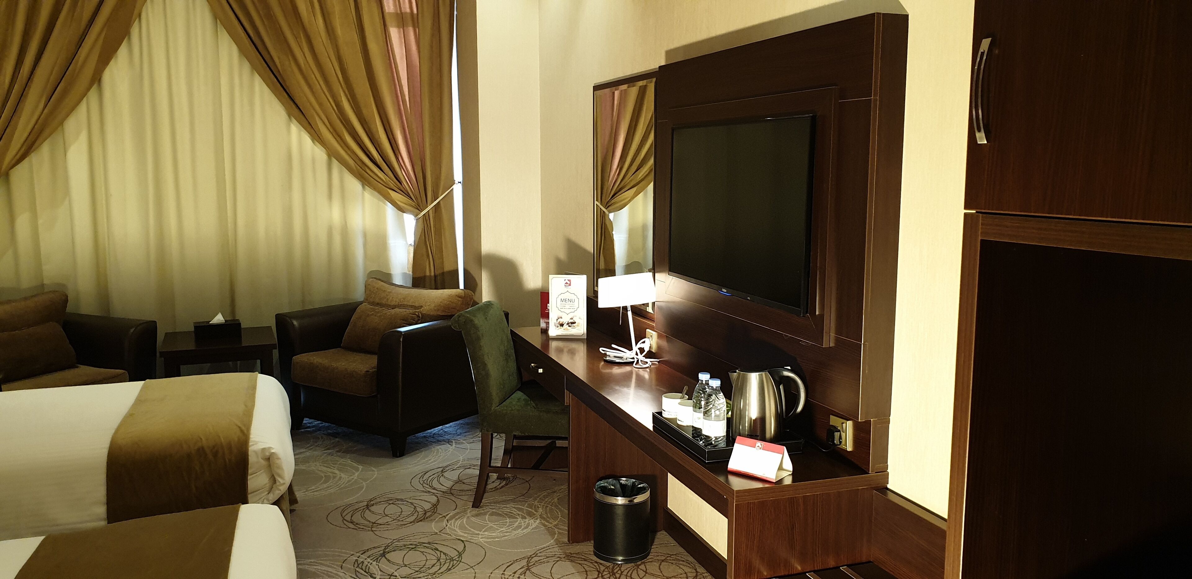 Ein Hotelzimmer mit Bett, Schreibtisch, Flachbildfernseher, Stuhl, kleinem Tisch und Mülleimer.