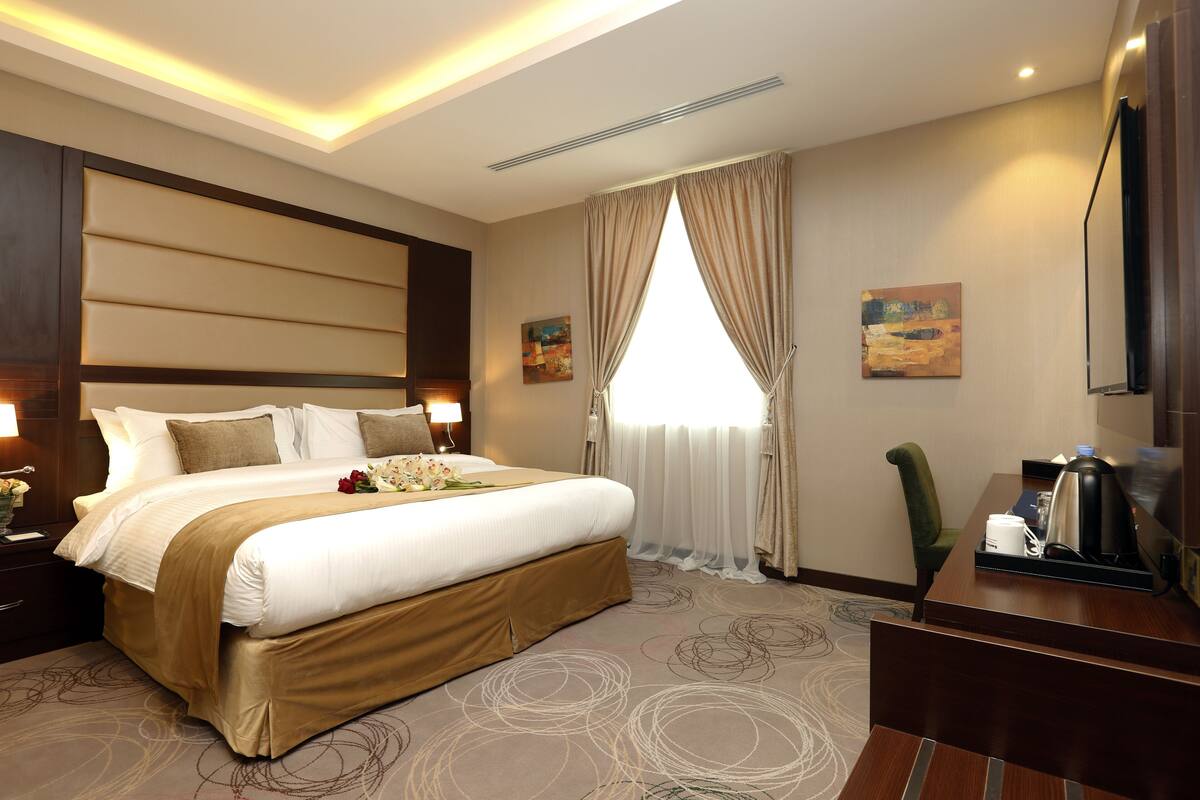 A hotel room with a large bed, a desk with a coffee maker, a TV, and a window with curtains.