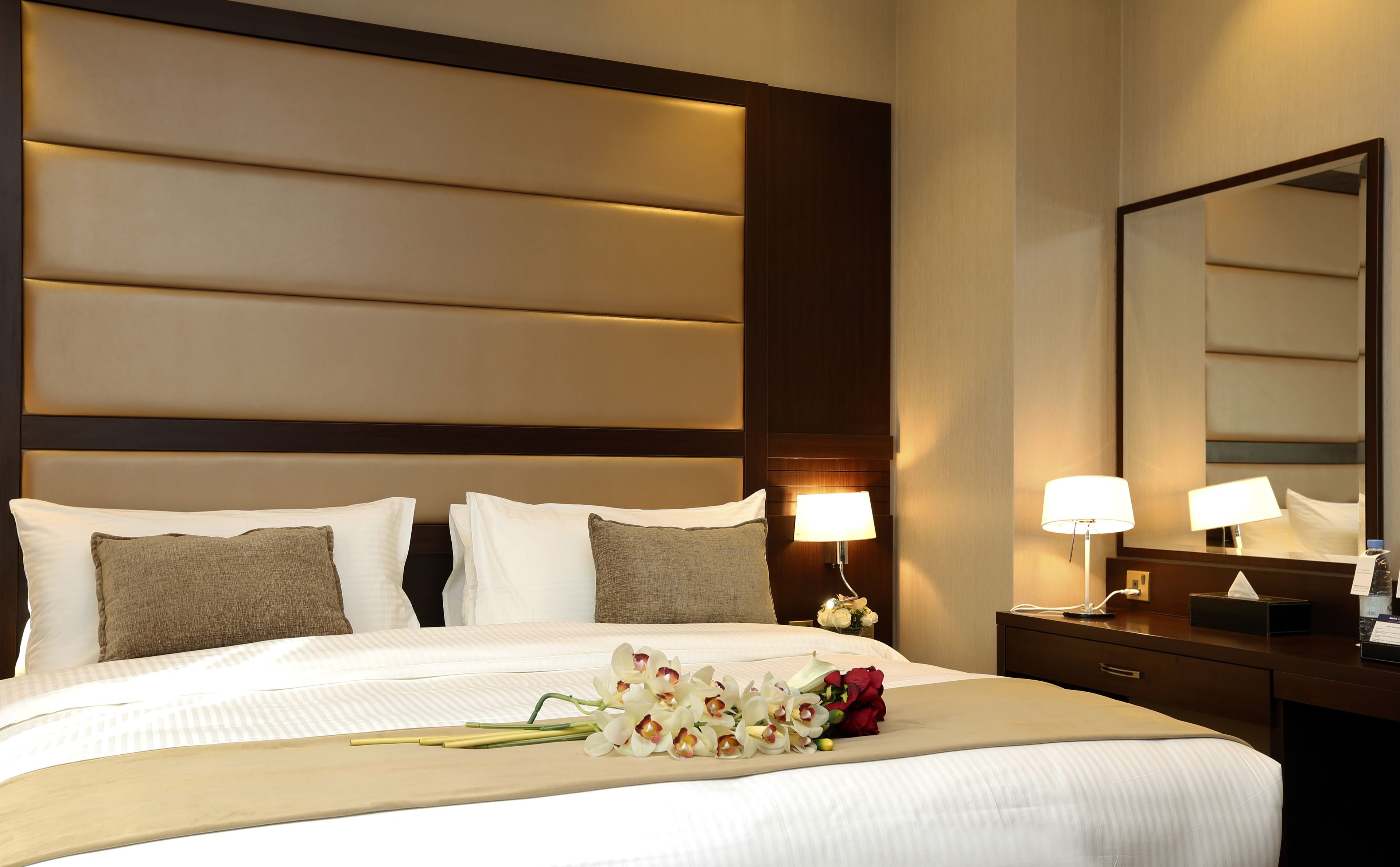 Une chambre d’hôtel avec un grand lit, deux lampes de chevet, une table de nuit, un miroir et un bouquet de fleurs sur le lit.