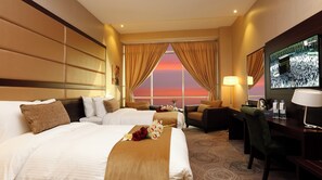 A hotel room with two beds, a desk, a chair, a TV, and a view of a sunset. - Swiss Flora Inn Hotel Riyadh (Riyadh)