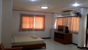 A room with a bed, a TV on a wooden stand, a fan, and an air conditioner. - Island Mansion (Krabi)