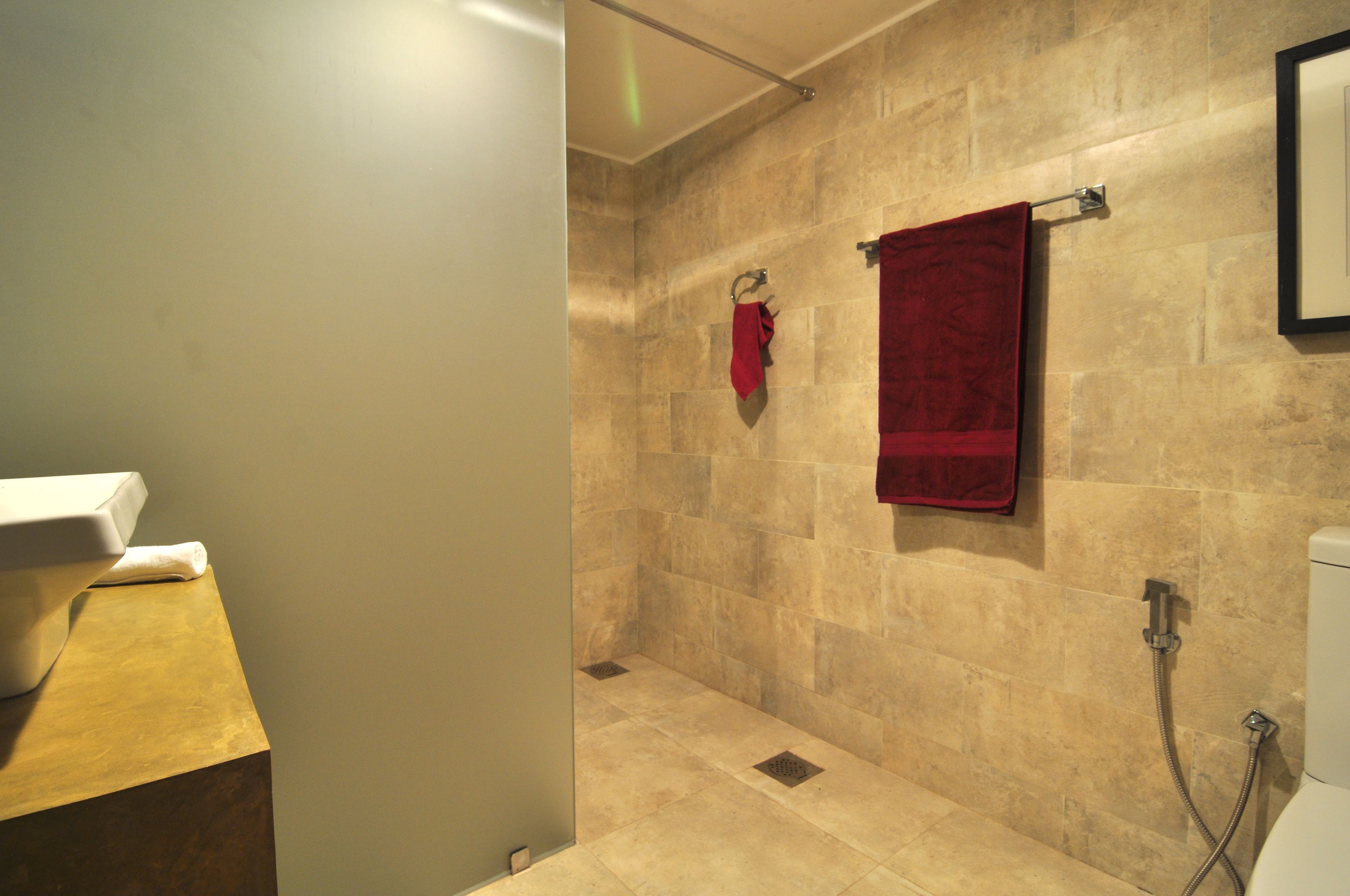 Un baño con pared de ducha en tonos beige, un lavamanos blanco y una toalla roja colgada en un perchero.