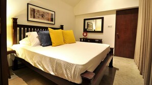 Un lit bien fait, avec une couette blanche et deux oreillers, une tête de lit en bois, une table de chevet avec une lampe, un tableau encadré au mur et une porte avec des rideaux.