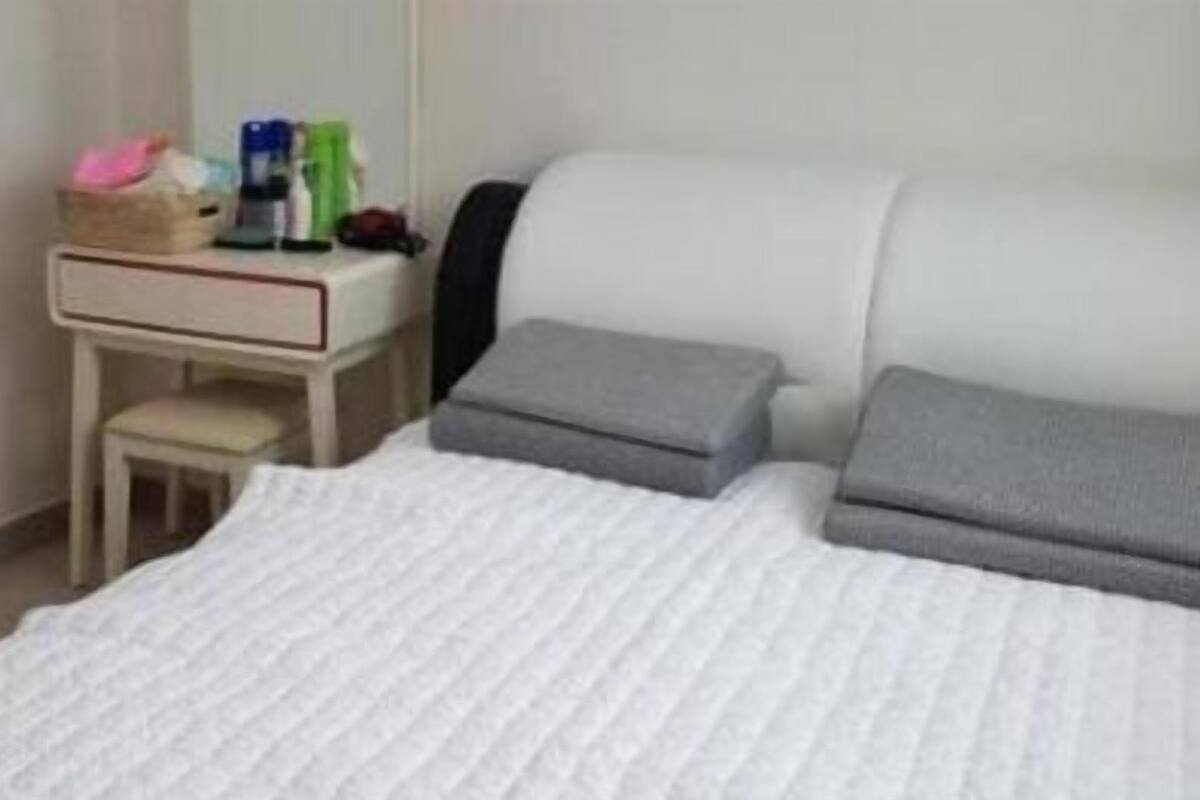 A neatly made bed with a white comforter and two pillows, a small bedside table with a lamp, and a chair.