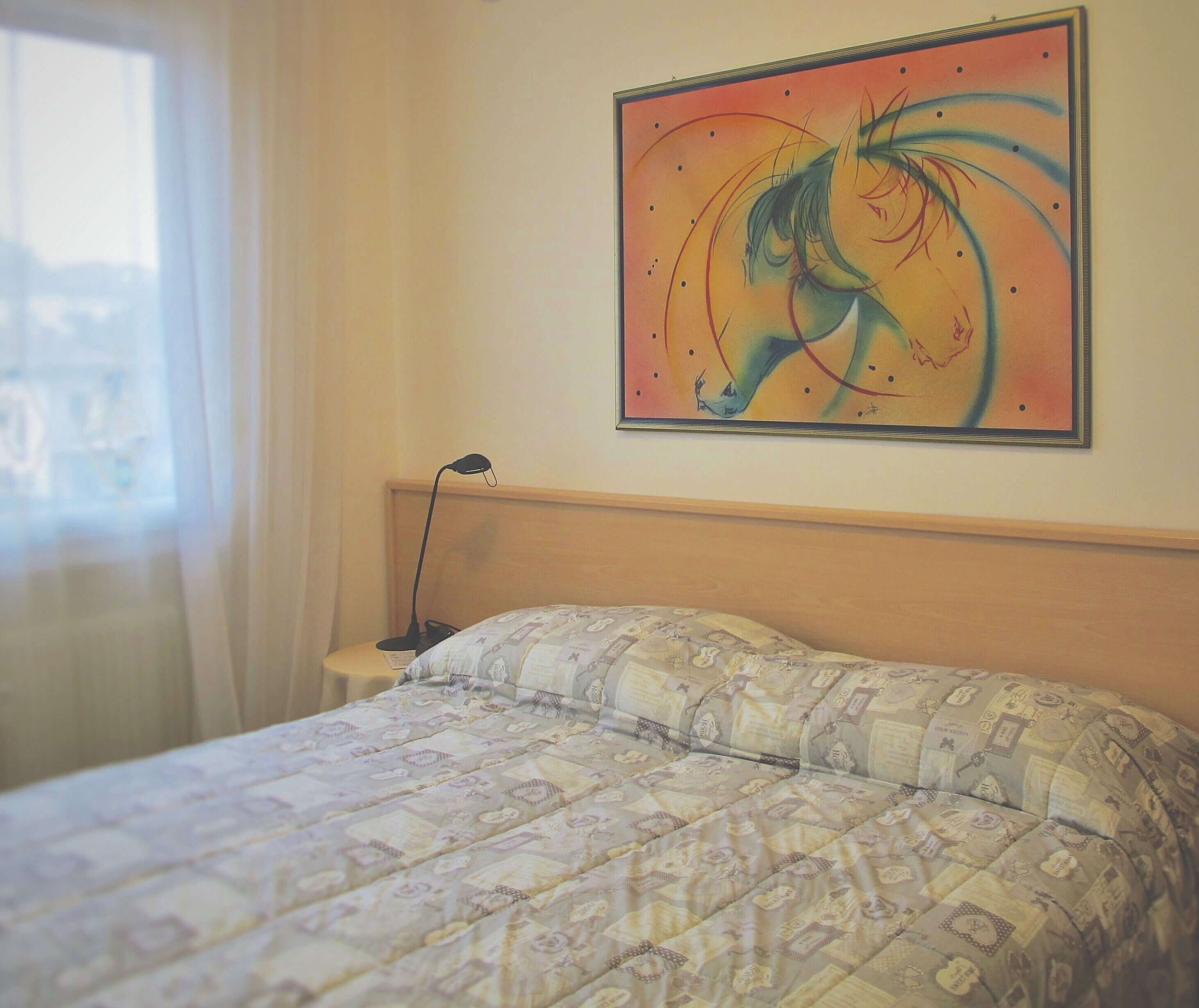 Una habitación de hotel con una cama, una mesita de noche, una lámpara y un cuadro en la pared.