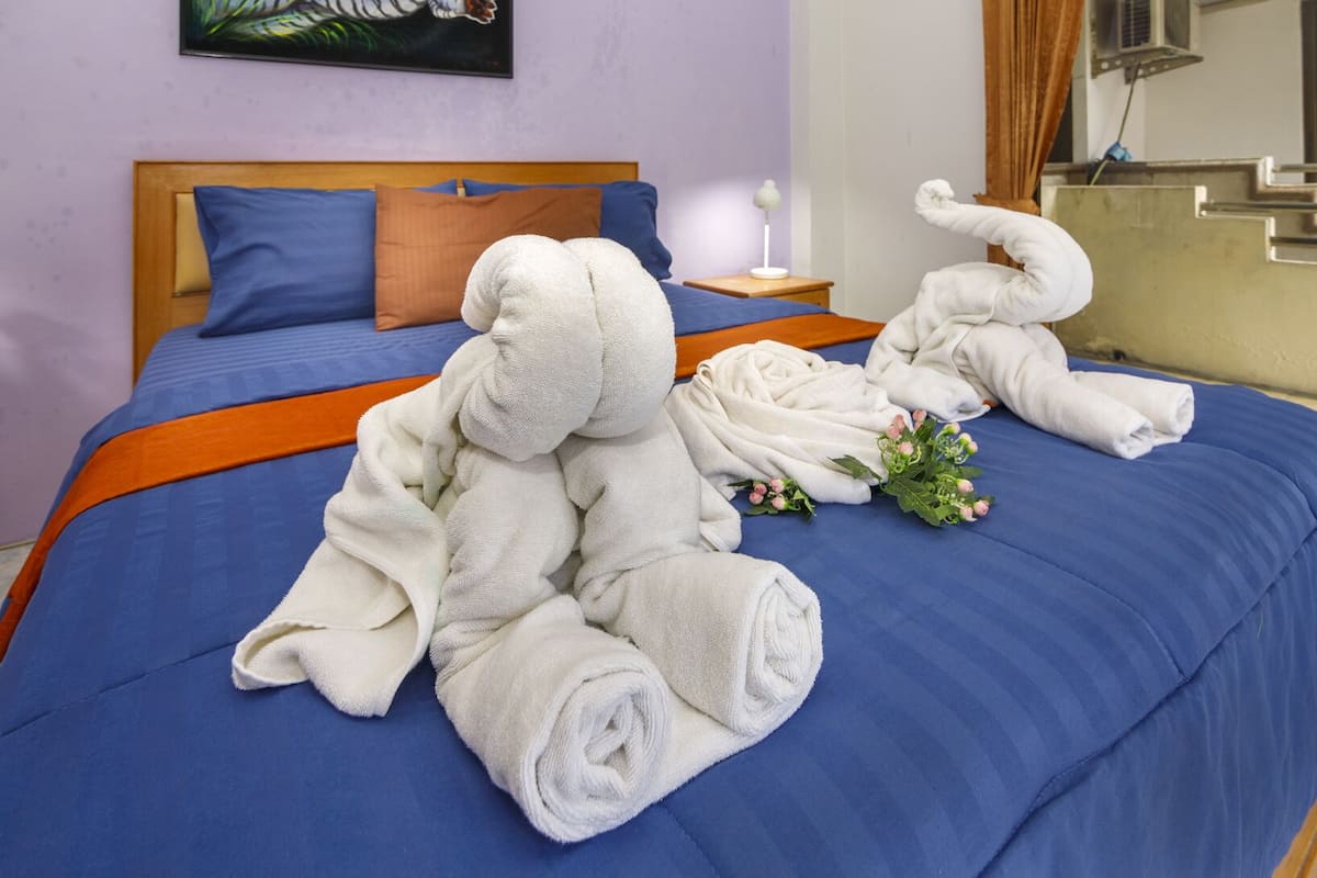Uma cama bem arrumada com roupa de cama azul e toalhas brancas, uma cabeceira de madeira e uma pequena mesa de cabeceira com um abajur.