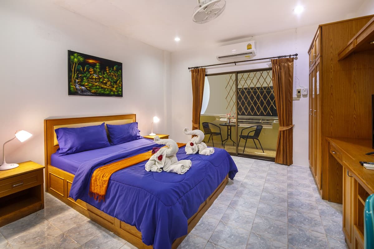 Quarto de hotel com cama, escrivaninha, cadeira, mesa pequena, um quadro e porta de correr para uma varanda.