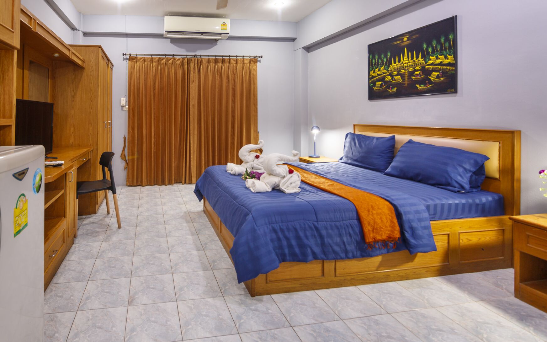 A hotel room with a bed, a desk, a chair, a refrigerator, and a curtain.