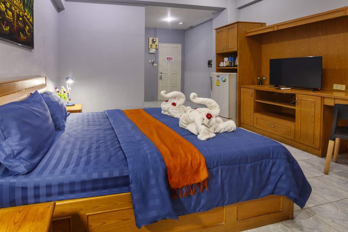 Quarto com cama, escrivaninha, televisão e banheiro ao fundo.