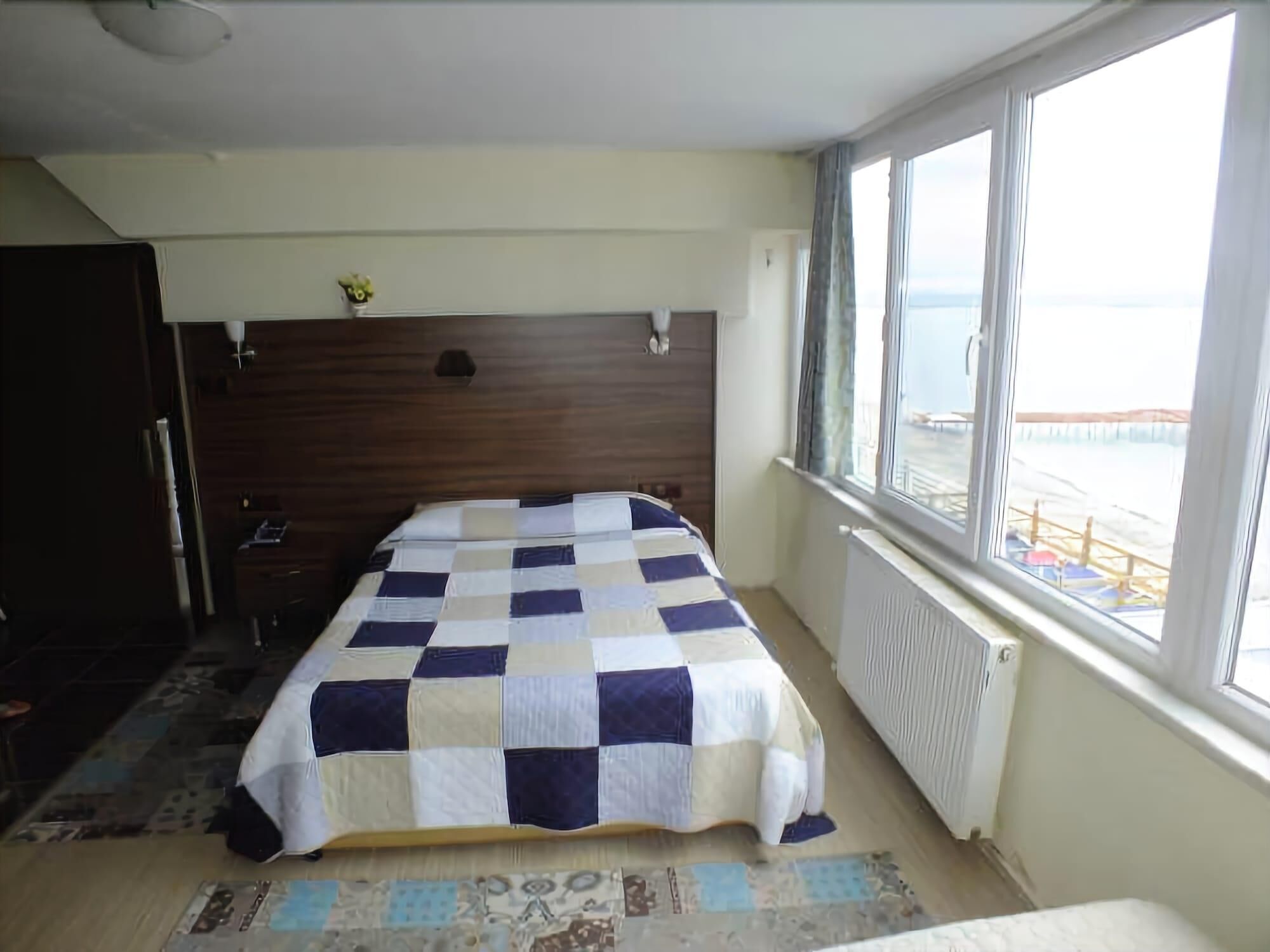 A bedroom with a checkered bedspread, a wooden headboard, a radiator, and a window with a view of the sea.