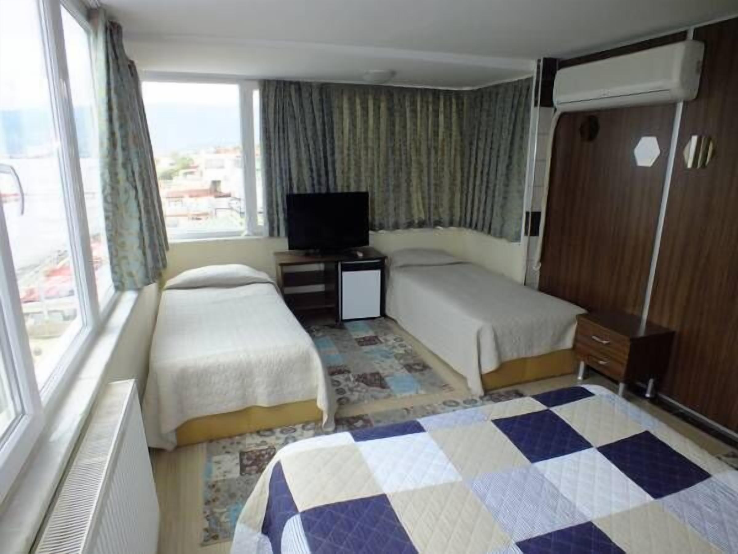 A hotel room with two beds, a television, a wardrobe, and a view of the city.