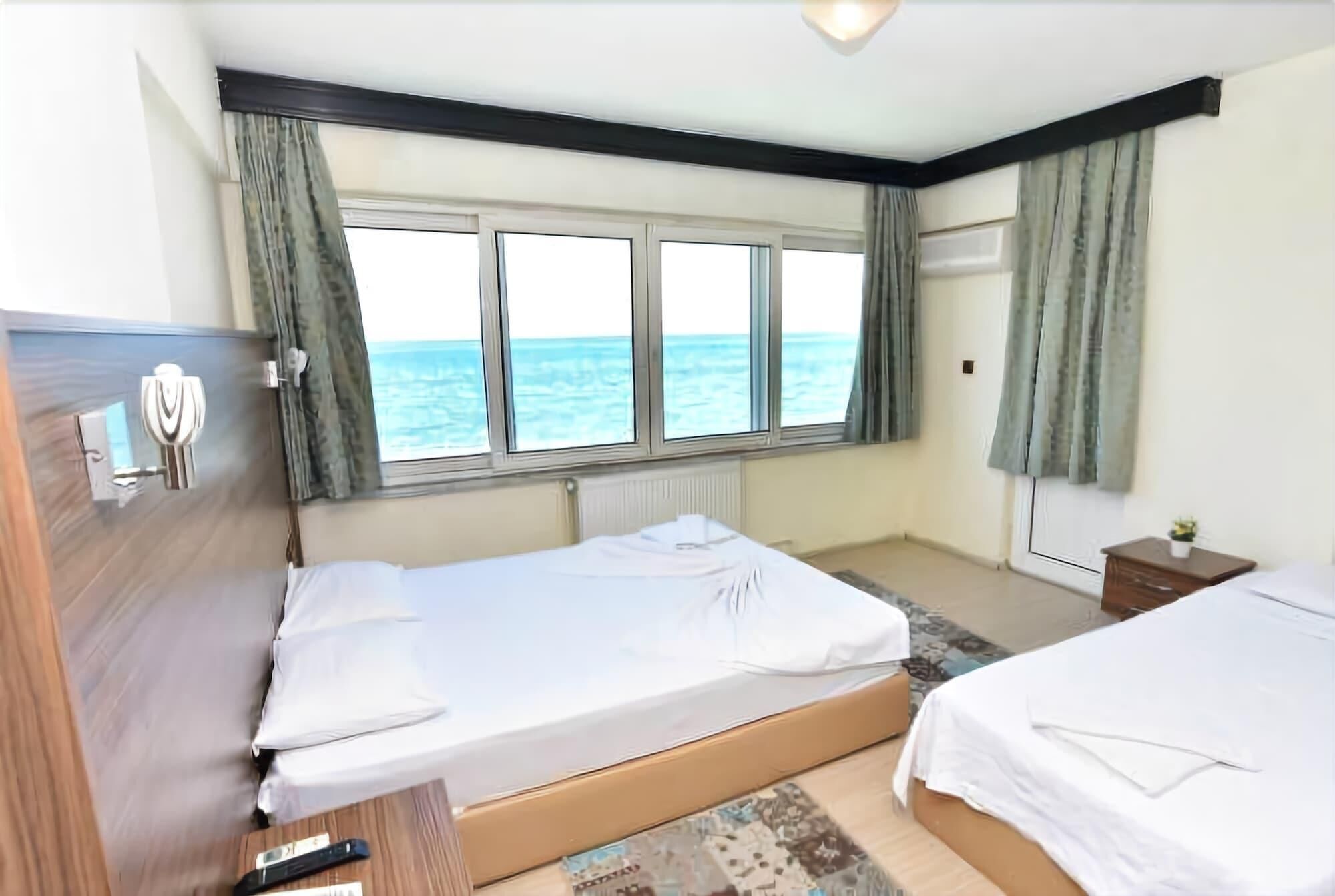 A bedroom with two beds, a window with a view of the sea, a wooden dresser, and a small table with a plant.