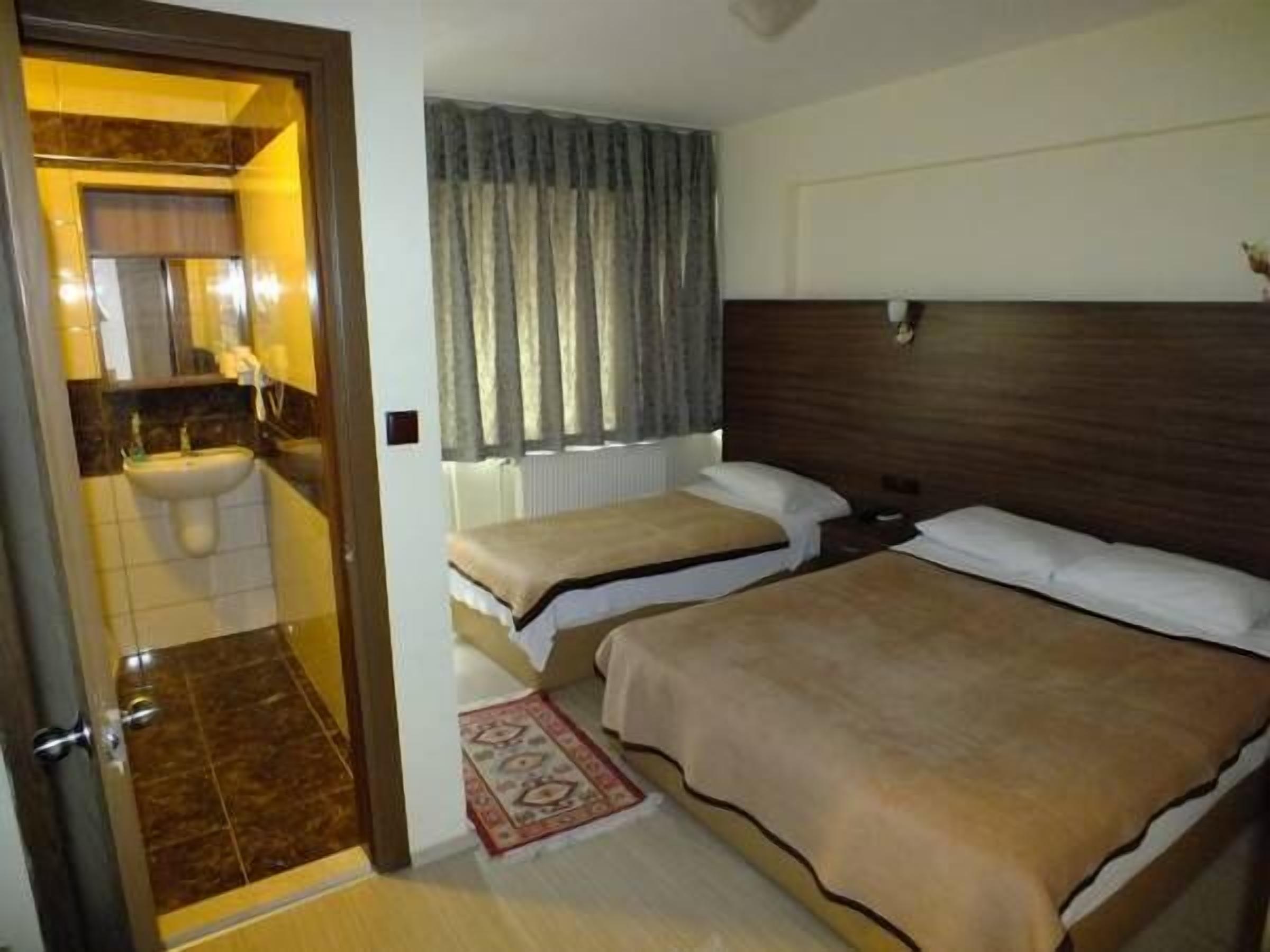 Habitación de hotel con cama, mesita de noche, espejo, ventana con cortinas y baño con lavamanos e inodoro.