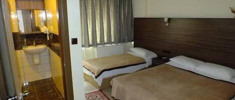 Habitación de hotel con cama, mesita de noche, espejo, ventana con cortinas y baño con lavamanos e inodoro.