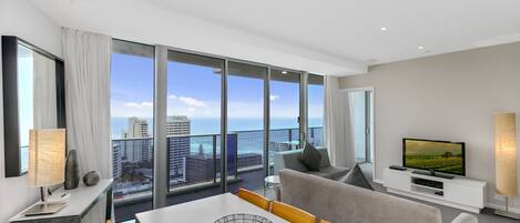 A modern hotel room with a balcony, large windows, a flat-screen TV, and a dining area.