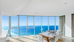 Un comedor moderno con una mesa grande y sillas, ventanas amplias con vistas al océano y un techo alto.