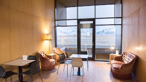 Un interior moderno con un ventanal amplio que ofrece vistas a un paisaje nevado. Hay varias opciones de asientos, incluyendo una mesa con sillas y un sofá.