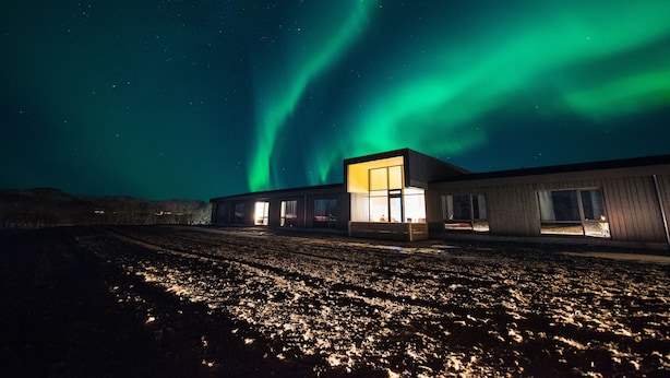 Un edificio con amplios ventanales y una puerta central de vidrio, con las auroras boreales como fondo.