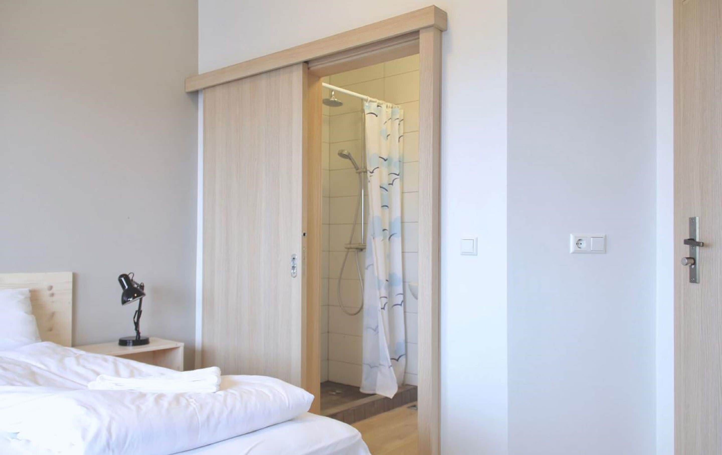 Un dormitorio con cama, lámpara de noche y puerta corredera que da a una zona de ducha con cortina.