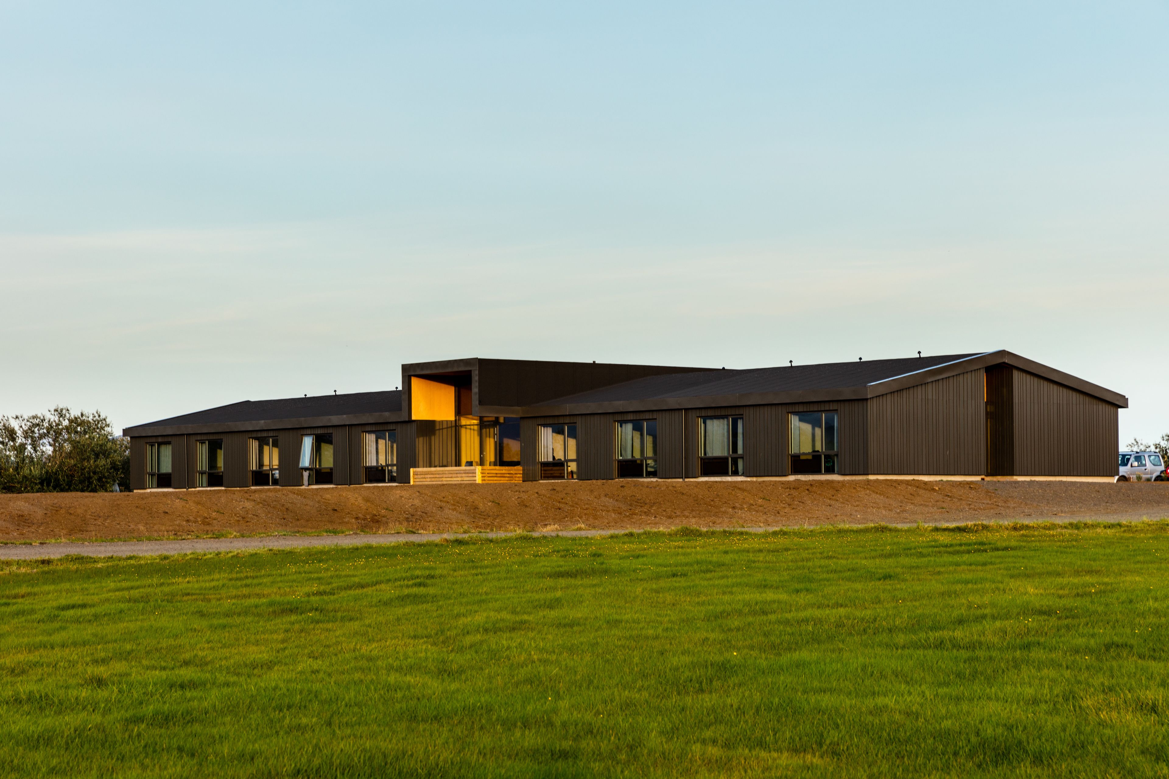 A modern building with a flat roof, large windows, and a grassy field in the foreground.