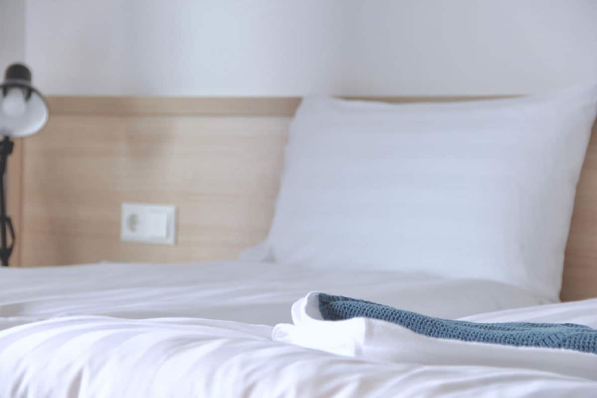 A neatly made bed with white linens and a blue knitted item on it.