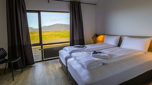 Habitación de hotel con dos camas, vistas a un paisaje montañoso, una silla y una lámpara.