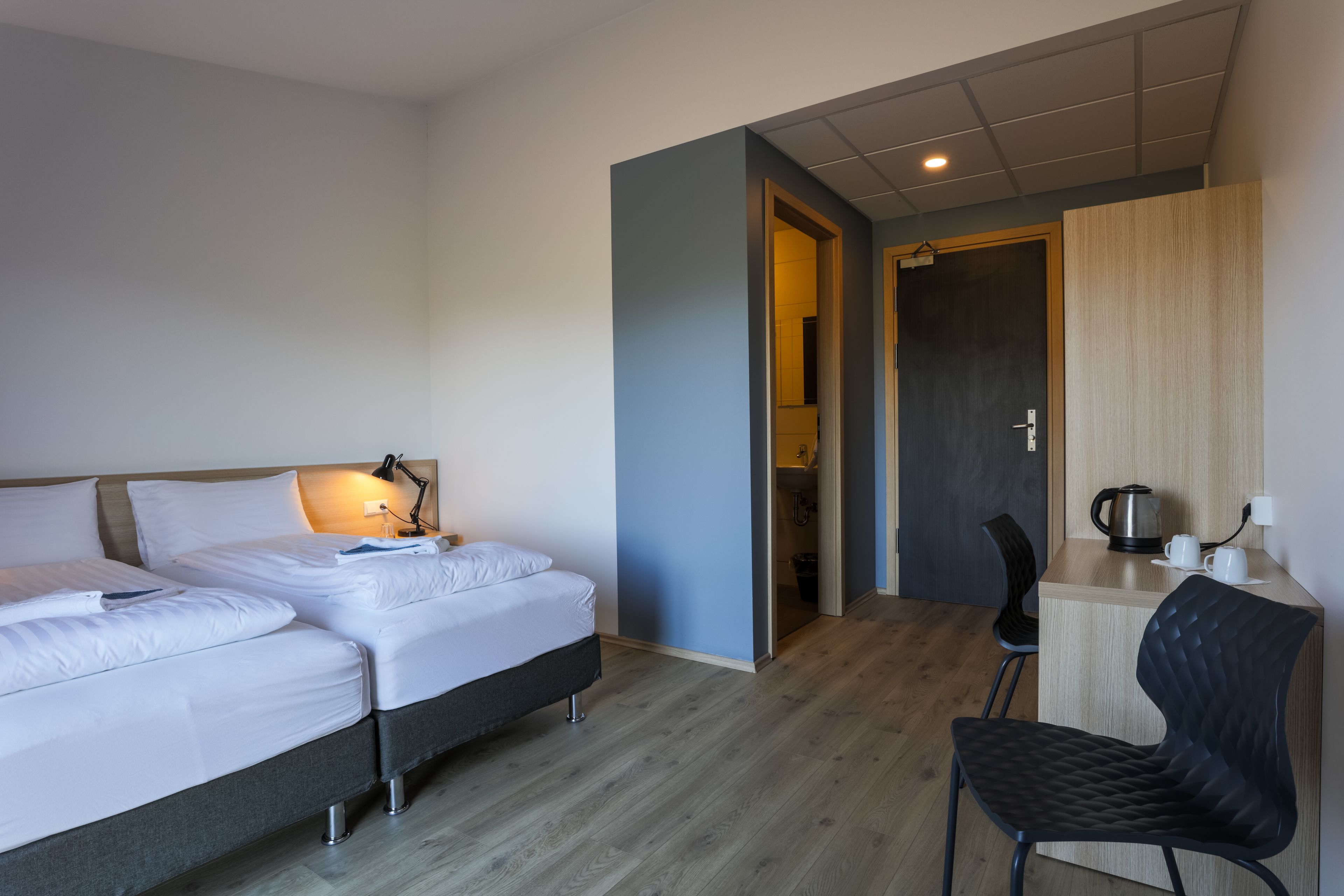 A hotel room with two beds, a desk with a chair, a coffee maker, and a shower area.