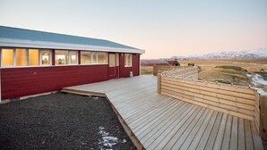Un edificio rojo con ventanas amplias, una terraza de madera y vistas a montañas nevadas.