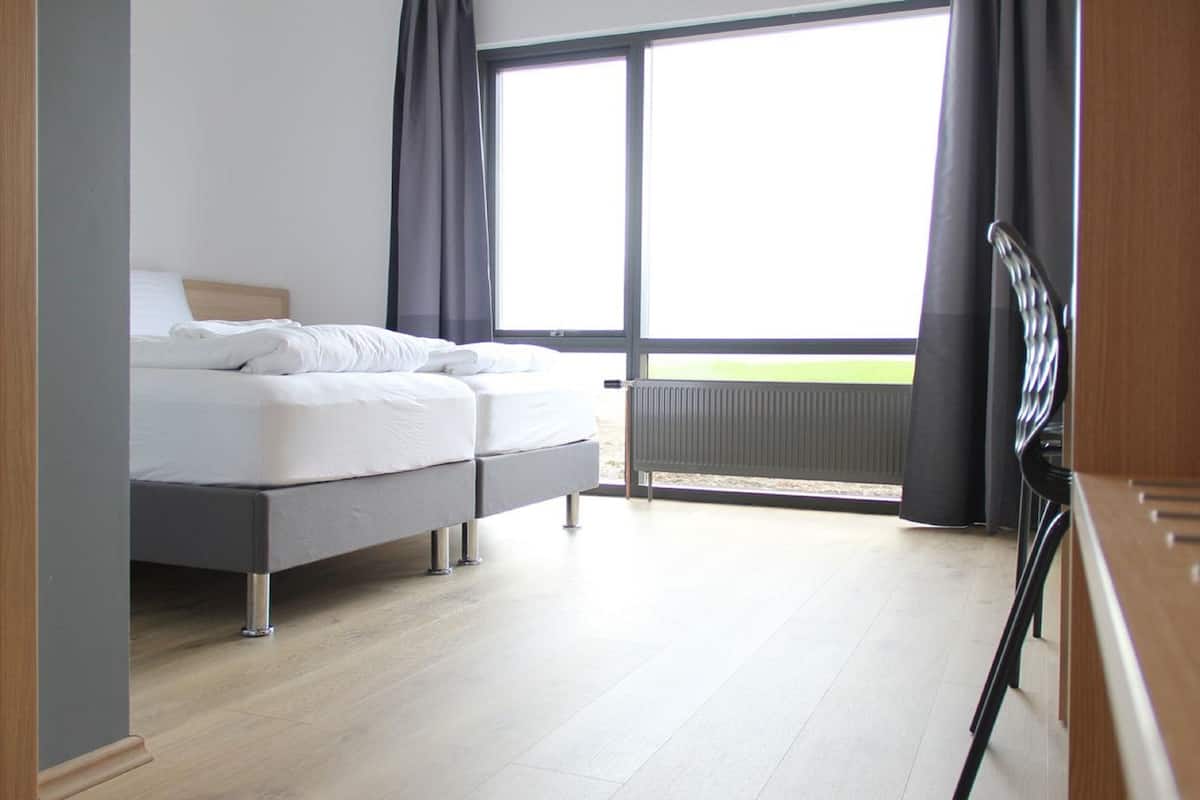 A modern bedroom with a bed, a view of the outdoors, and a large window.