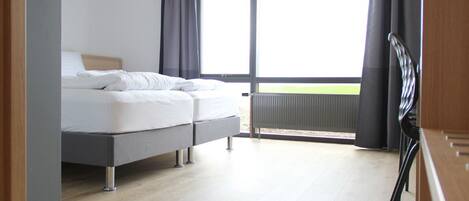 A modern bedroom with a bed, a view of the outdoors, and a large window.
