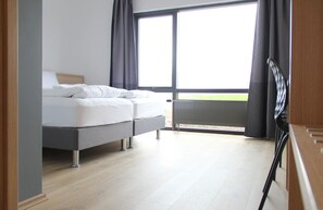 A modern bedroom with a bed, a view of the outdoors, and a large window.