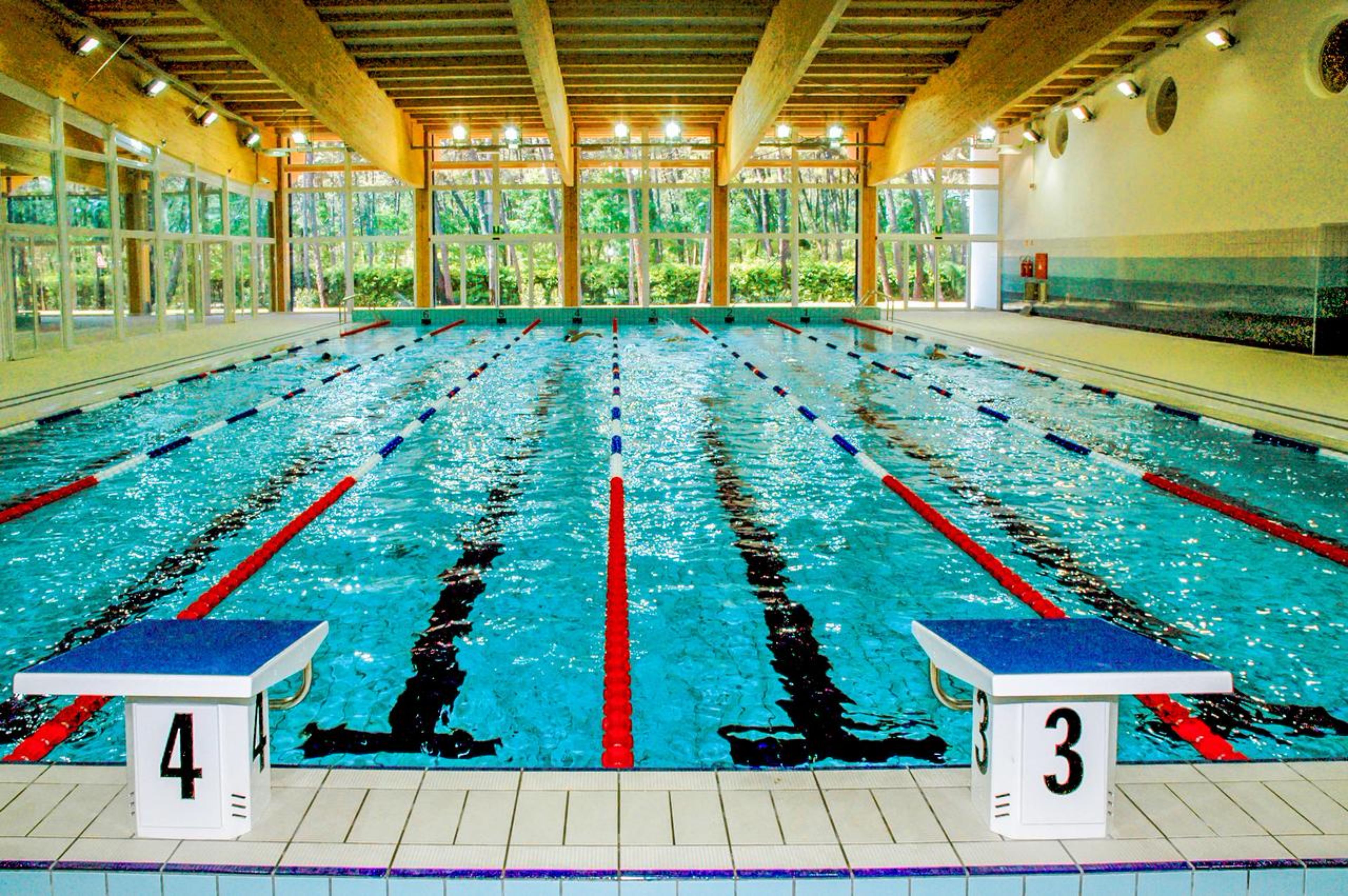 An indoor swimming pool with lanes marked by red and blue dividers, numbered 3 and 4, and a tiled floor.