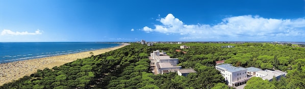 Zona costera con playa, abundante vegetación y varios edificios.