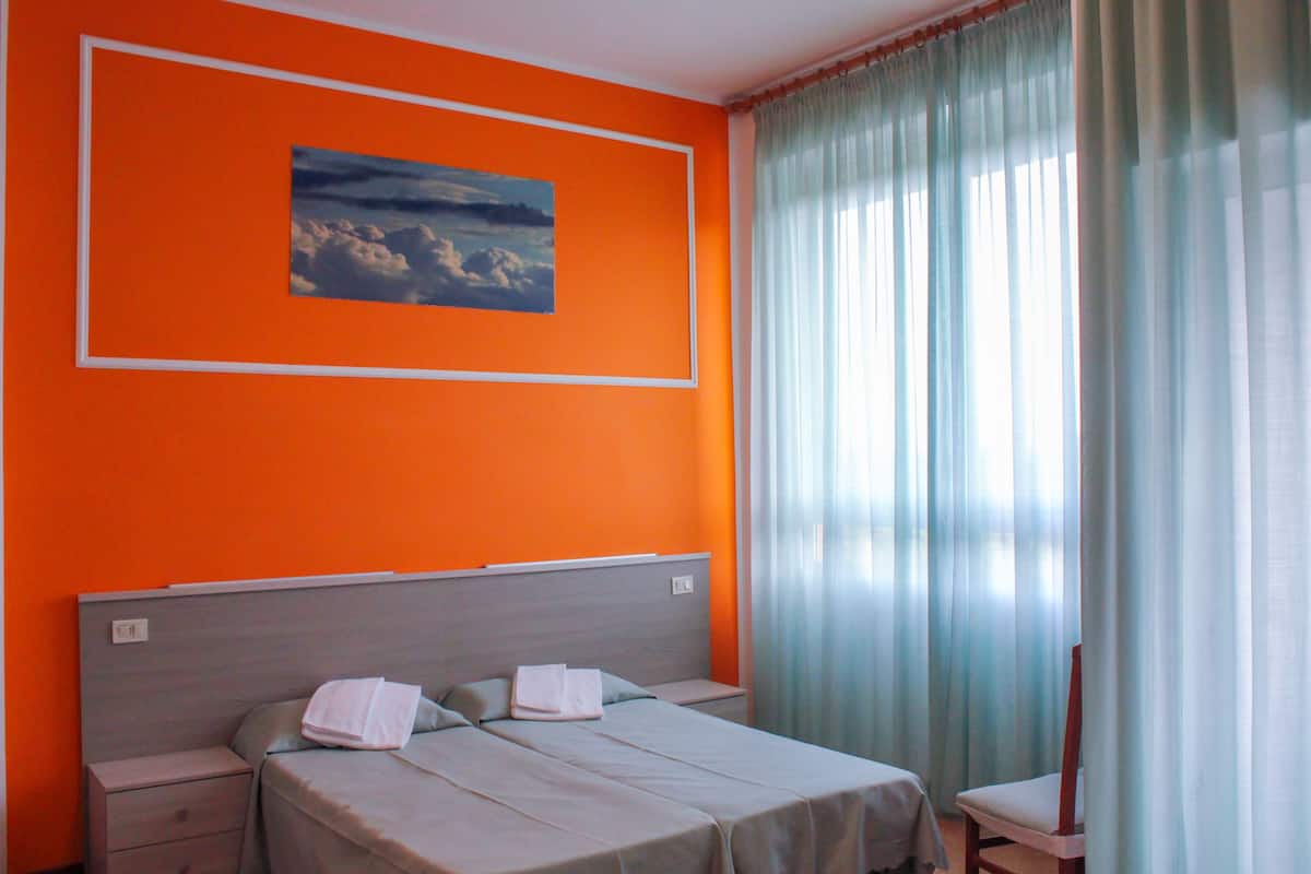 A hotel room with a bed, a nightstand, a chair, and a window with curtains.