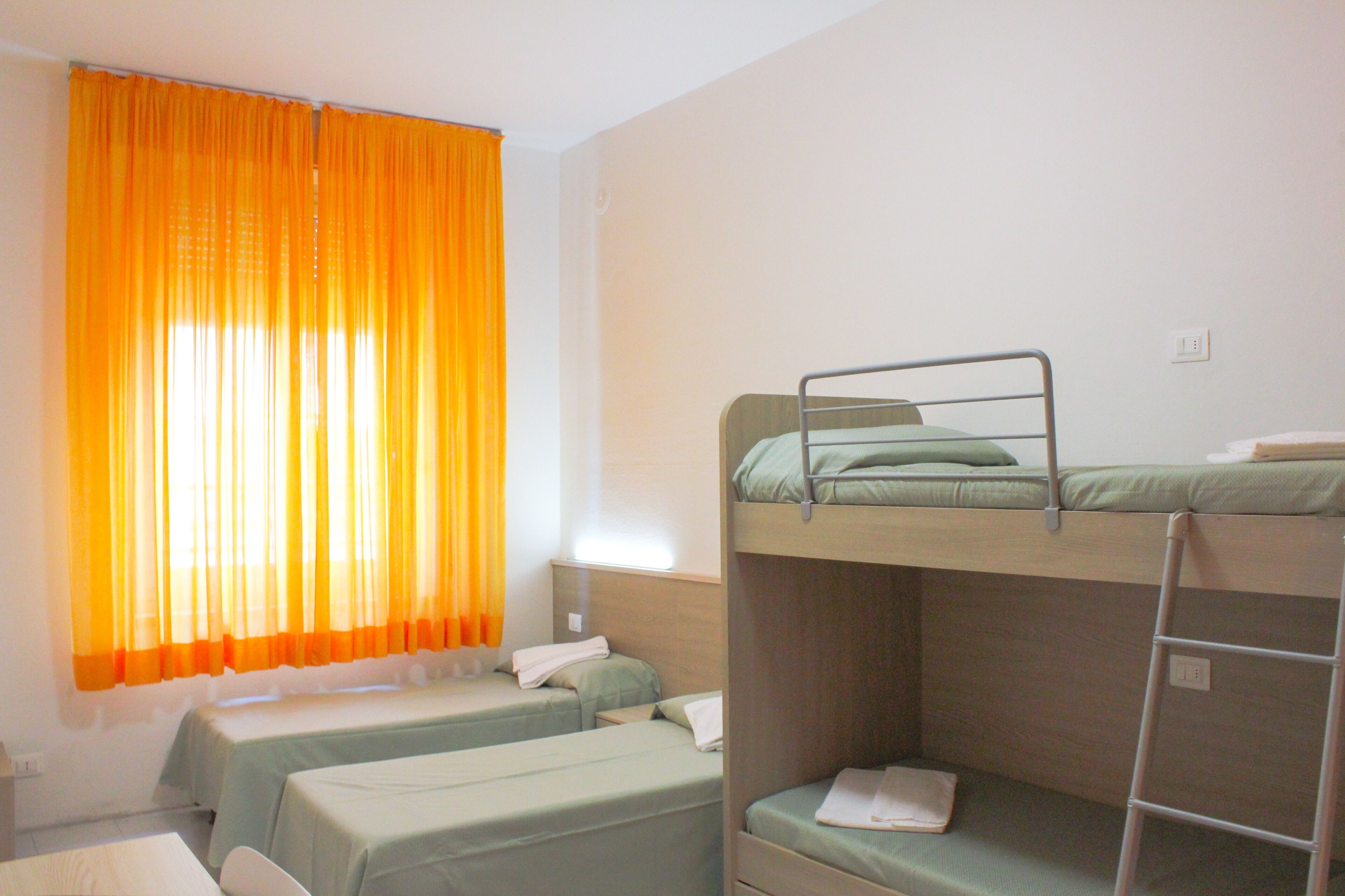 Una habitación con literas, una ventana con cortinas naranjas y una pared blanca.
