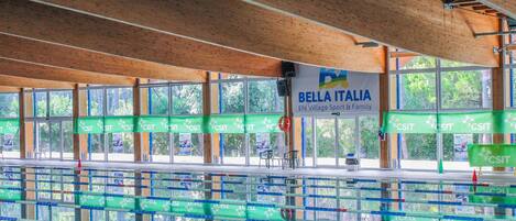 A swimming pool area with multiple lanes, wooden beams on the ceiling, and a banner reading "Bella Italia".