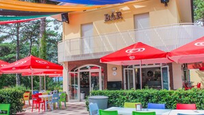 Un espacio al aire libre con sillas y mesas coloridas, sombrillas y un edificio con un letrero que dice 'BAR'.