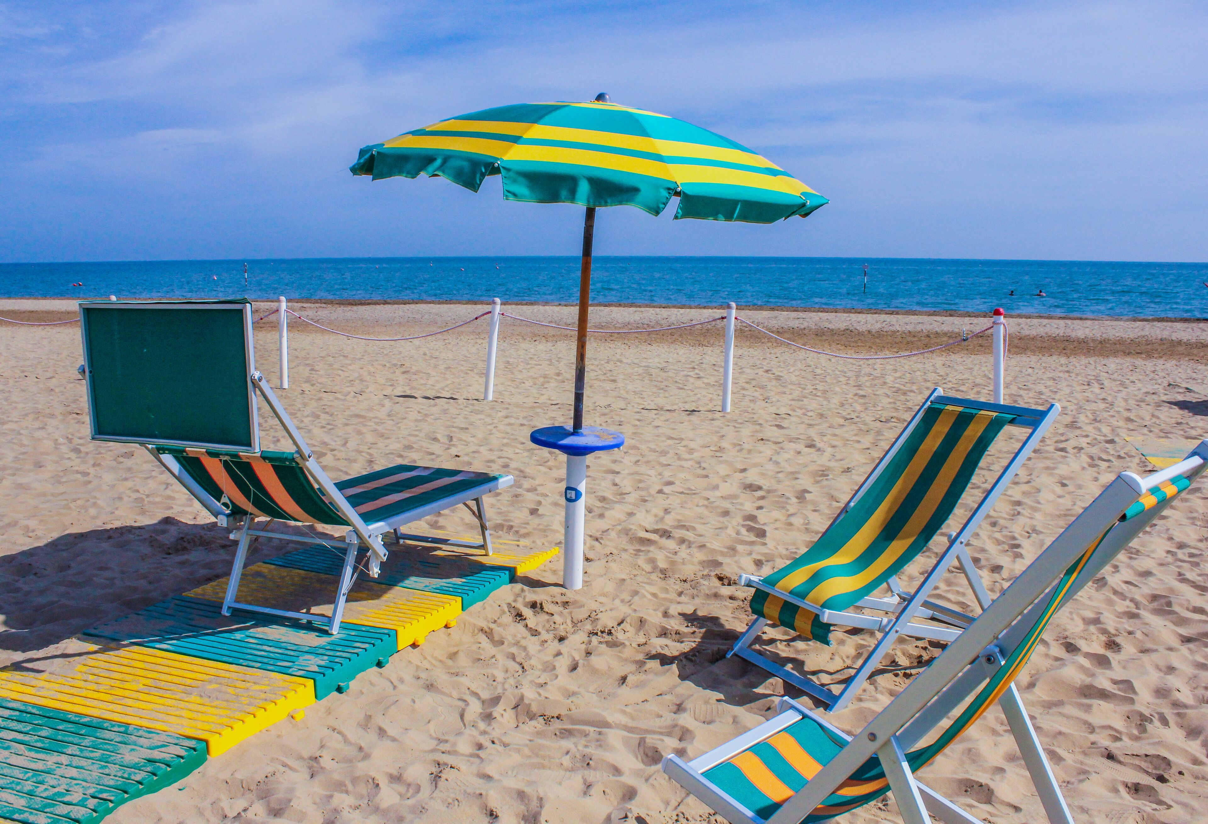 Ein Strand mit zwei gestreiften Liegestühlen und einem grünen Sonnenschirm.