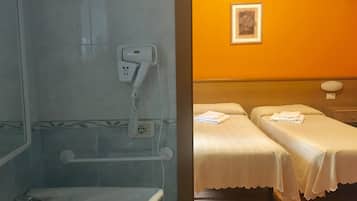Ein Badezimmer mit Dusche, Toilette und einem Föhn, der an einer Wandsteckdose befestigt ist. Ein Bett mit weißer Bettdecke und ein gerahmtes Bild an der Wand sind ebenfalls vorhanden.