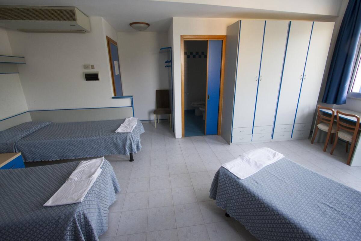 A hotel room with two single beds, a wardrobe, a chair, and a bathroom visible through an open door.