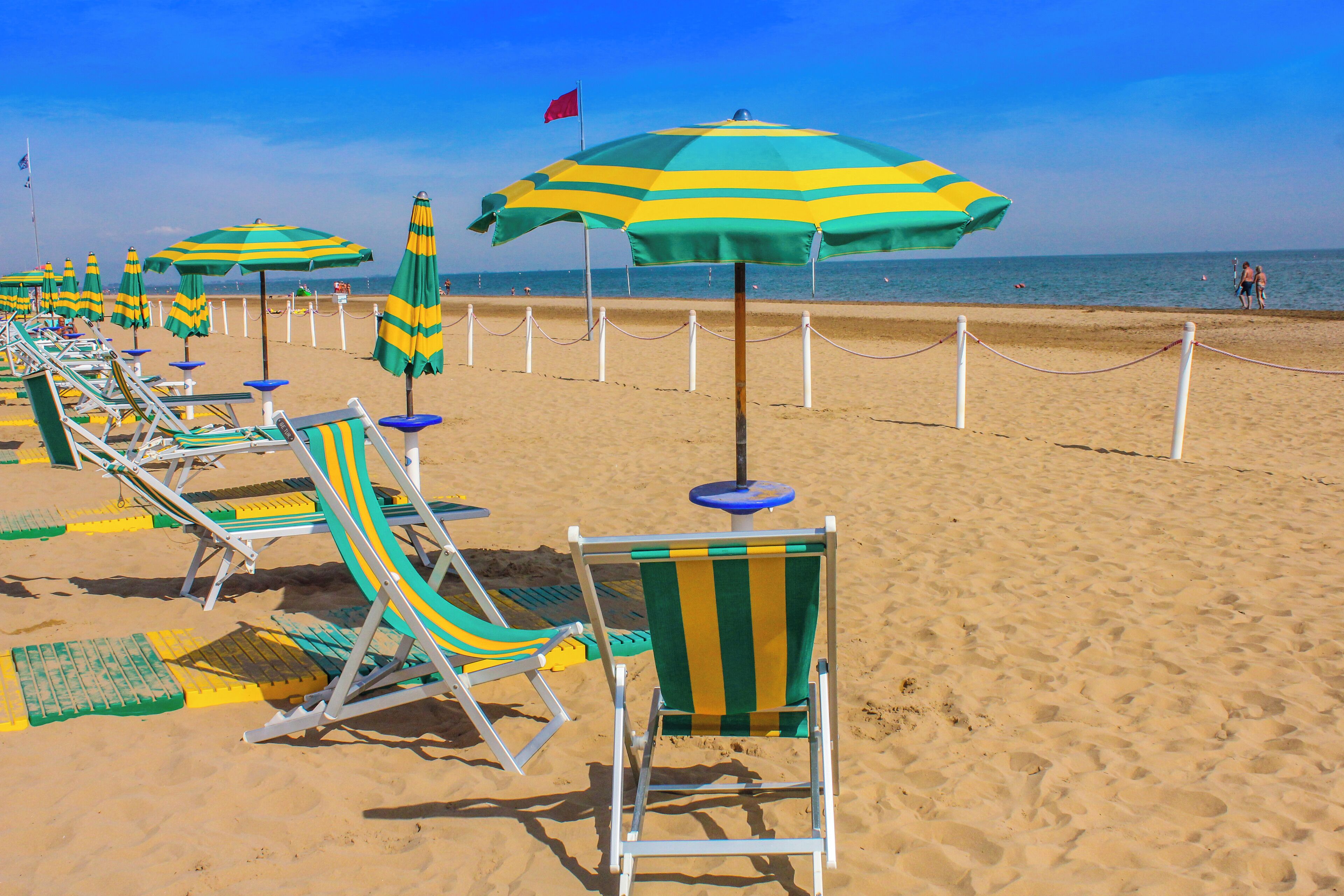 A beach with rows of beach chairs and umbrellas, a sandy shore, and a clear sky.
