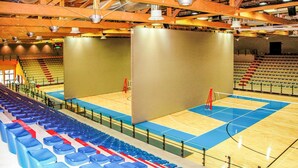Un espacio interior para deportes con cancha de baloncesto, zonas de asientos y un escenario o área para presentaciones.