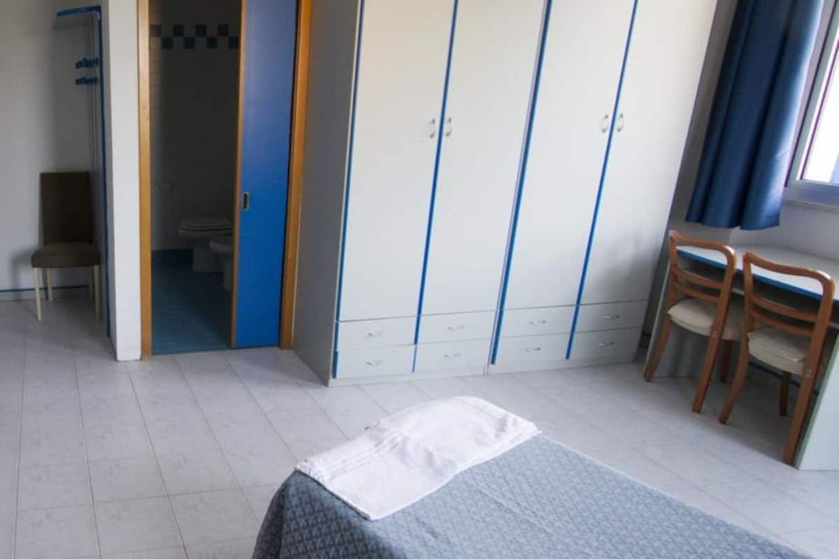 A bedroom with a bed, a wardrobe, a chair, and a bathroom visible through an open door.