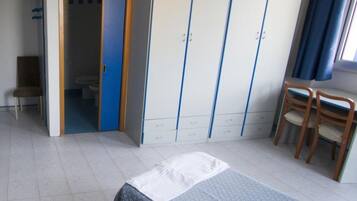 Un dormitorio con una cama, un armario, una silla y un baño visible a través de una puerta abierta.