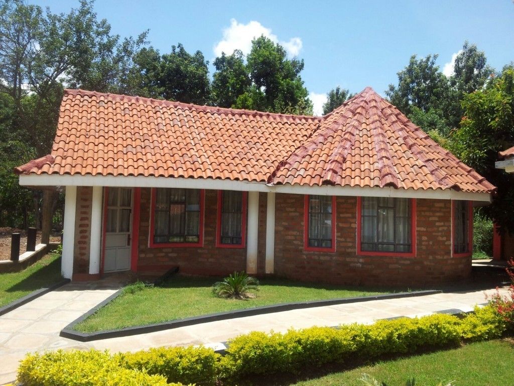 Um edifício de dois andares em tijolo, com telhado de telhas vermelhas, várias janelas com molduras vermelhas e uma pequena área de jardim na frente.